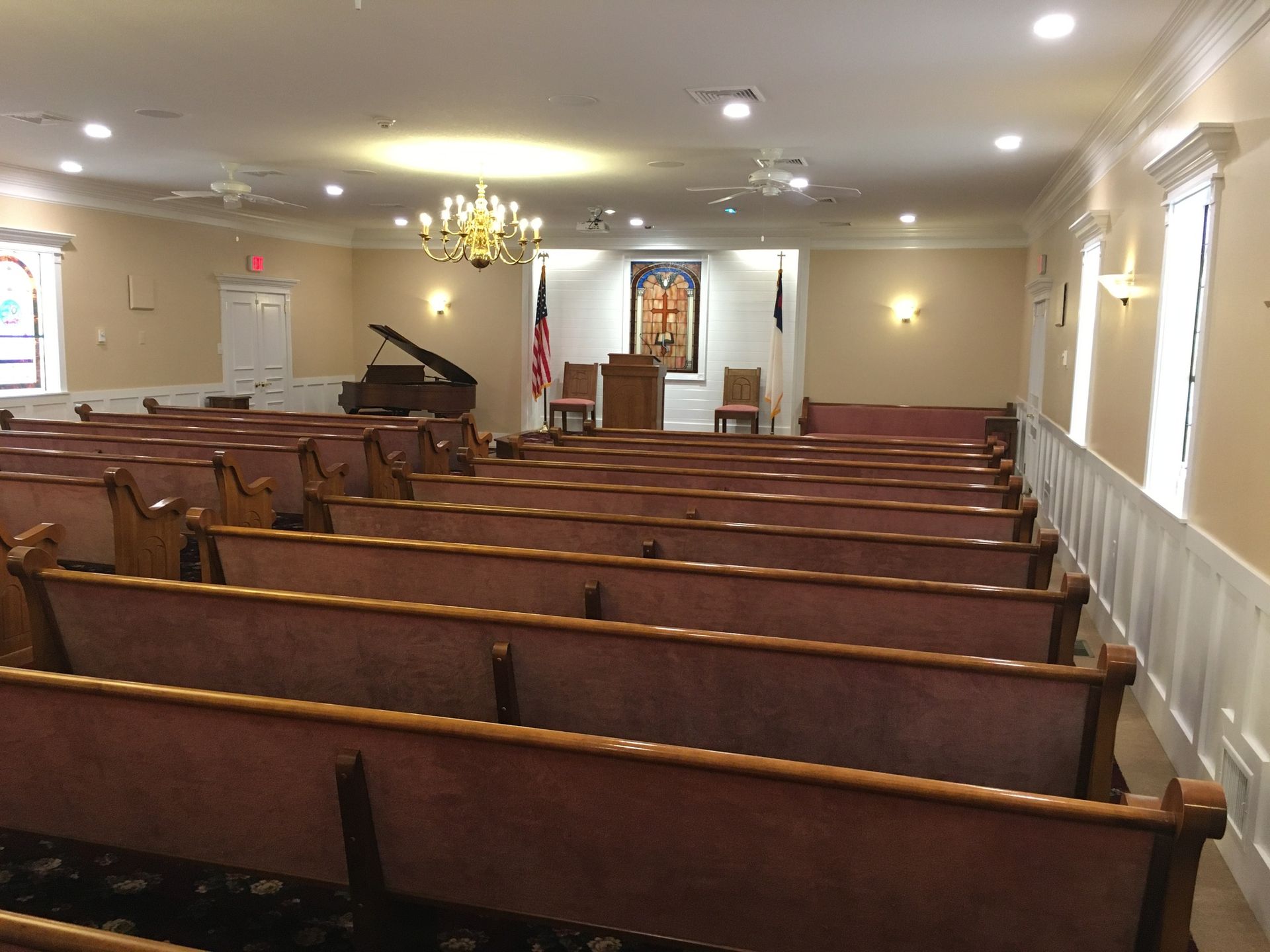 Empty church sanctuary with wooden pews facing the altar, piano, and stained glass window