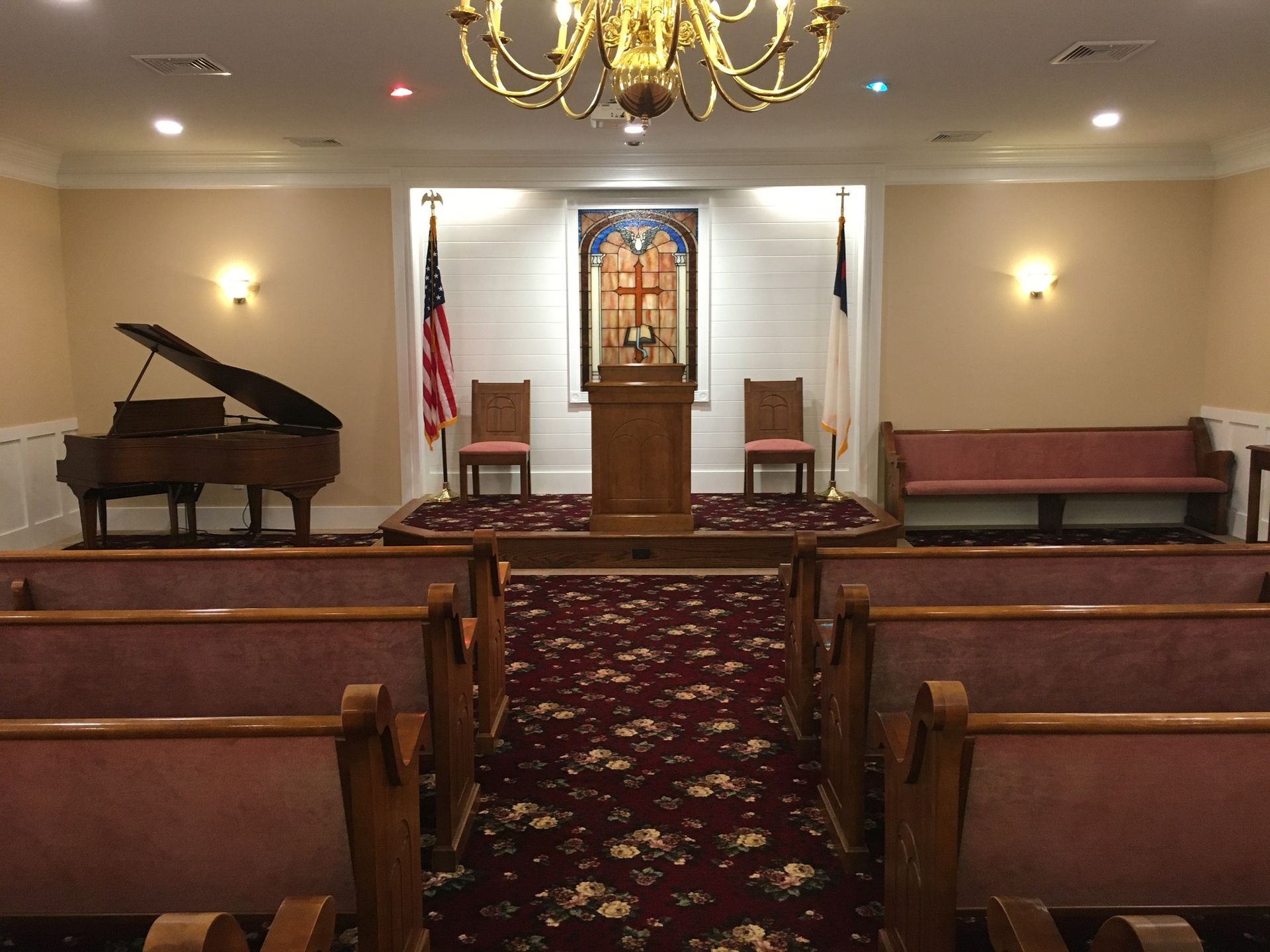 Small church sanctuary with wooden pews, a pulpit, American flag, piano, and chandelier under warm lights