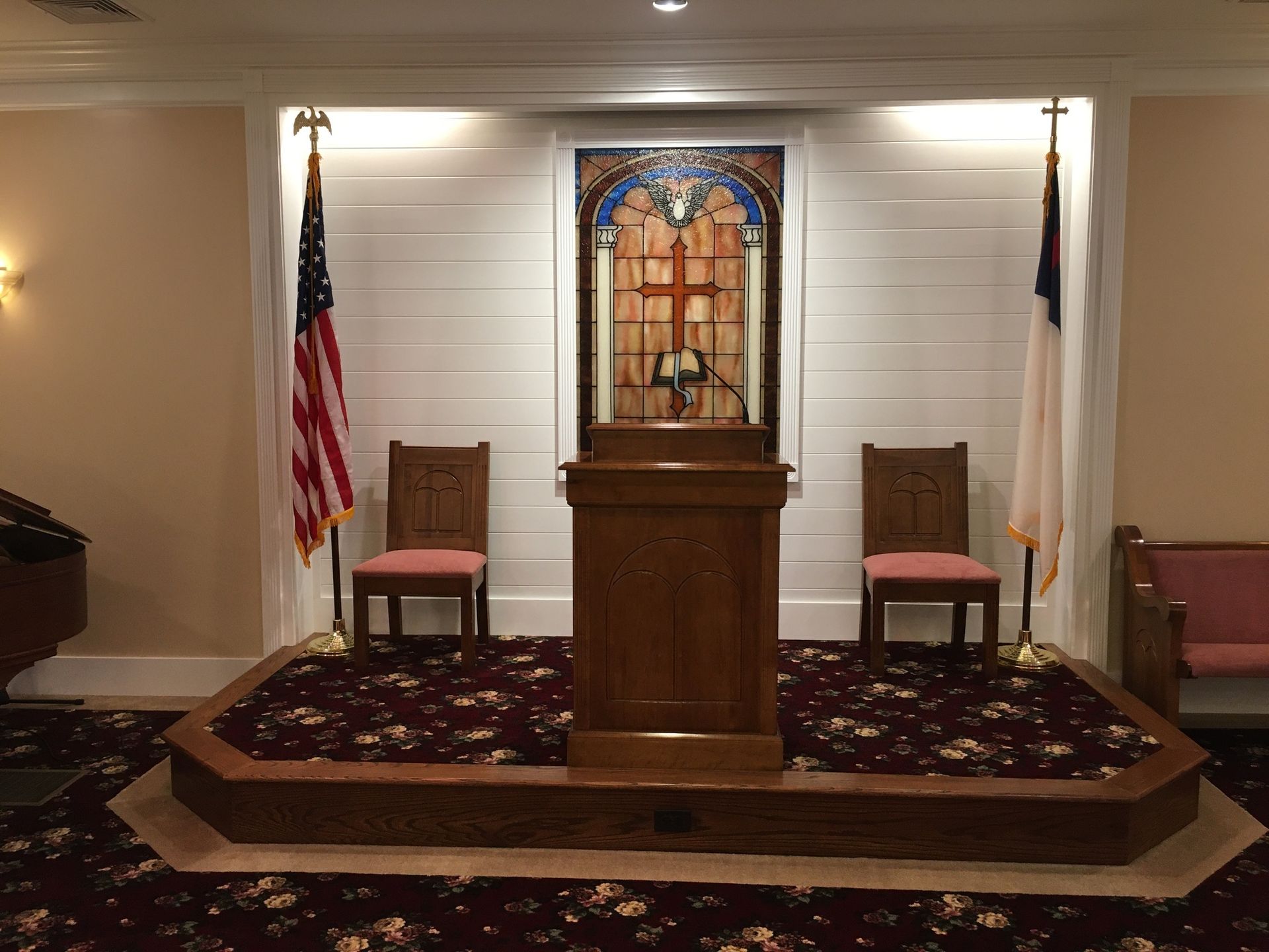 Church pulpit on a raised platform with chairs, American and Christian flags, and a stained-glass cross panel