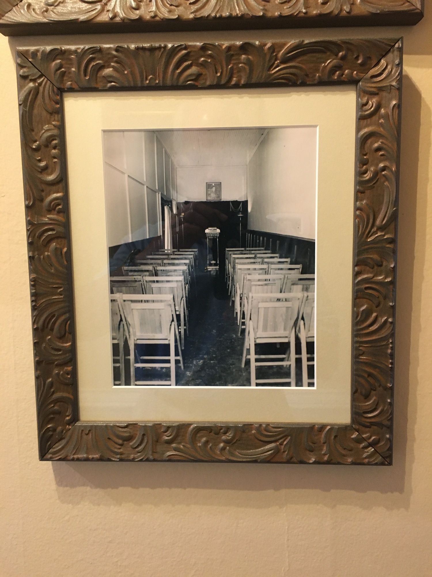 Framed black-and-white photo of a small chapel aisle with rows of white chairs and an altar at the back