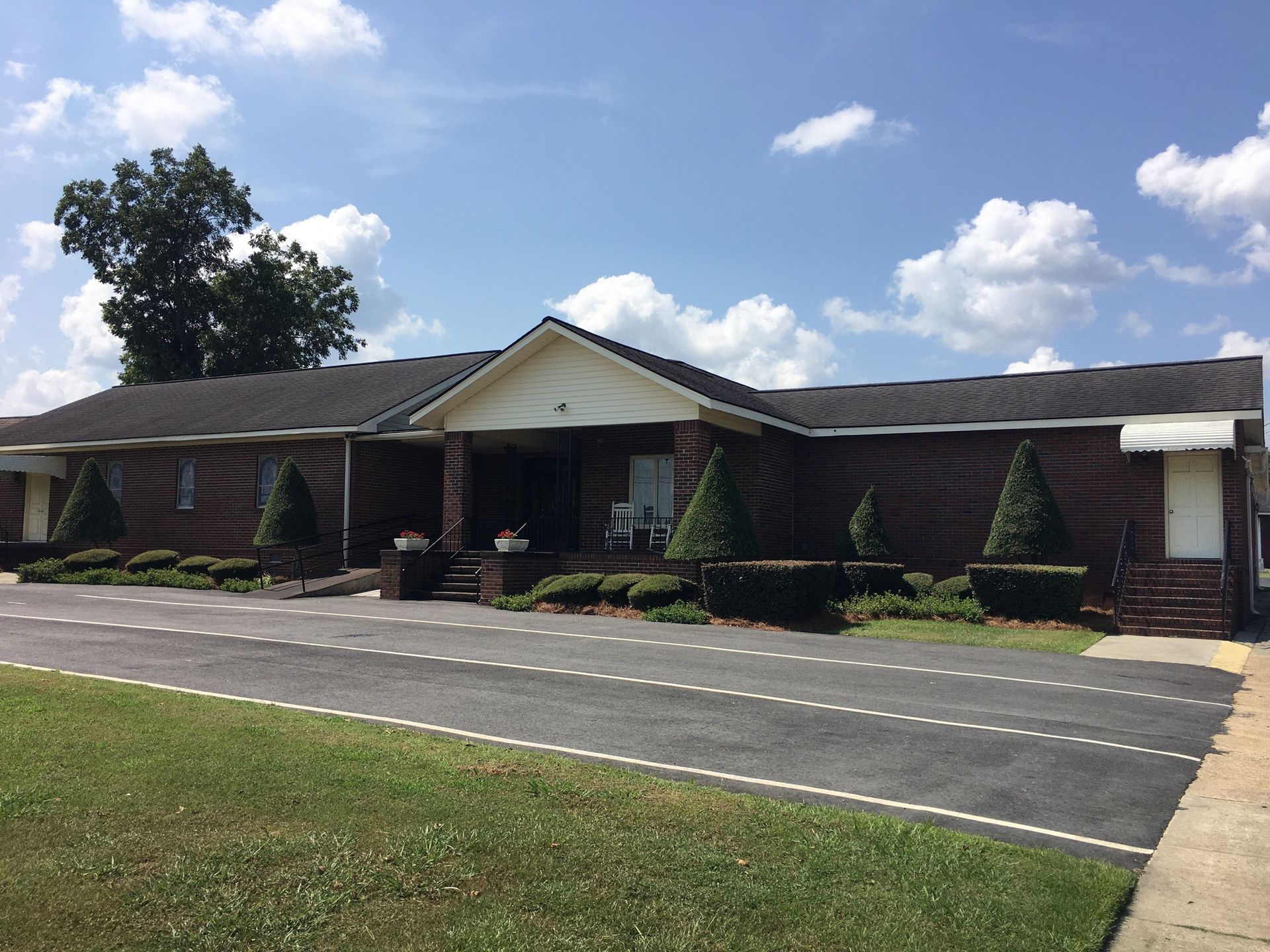 Single-story brick building with a covered entrance, driveway, and landscaped lawn under a blue sky