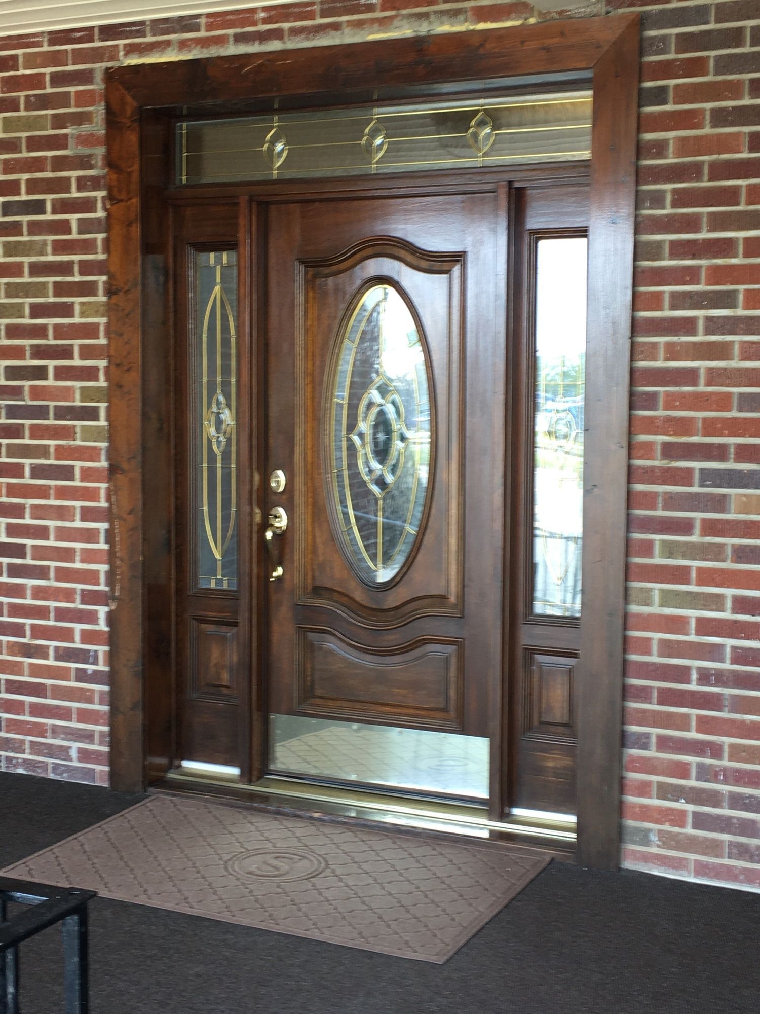 Wooden front door with oval glass insert set in a brick entryway, beside narrow sidelights.