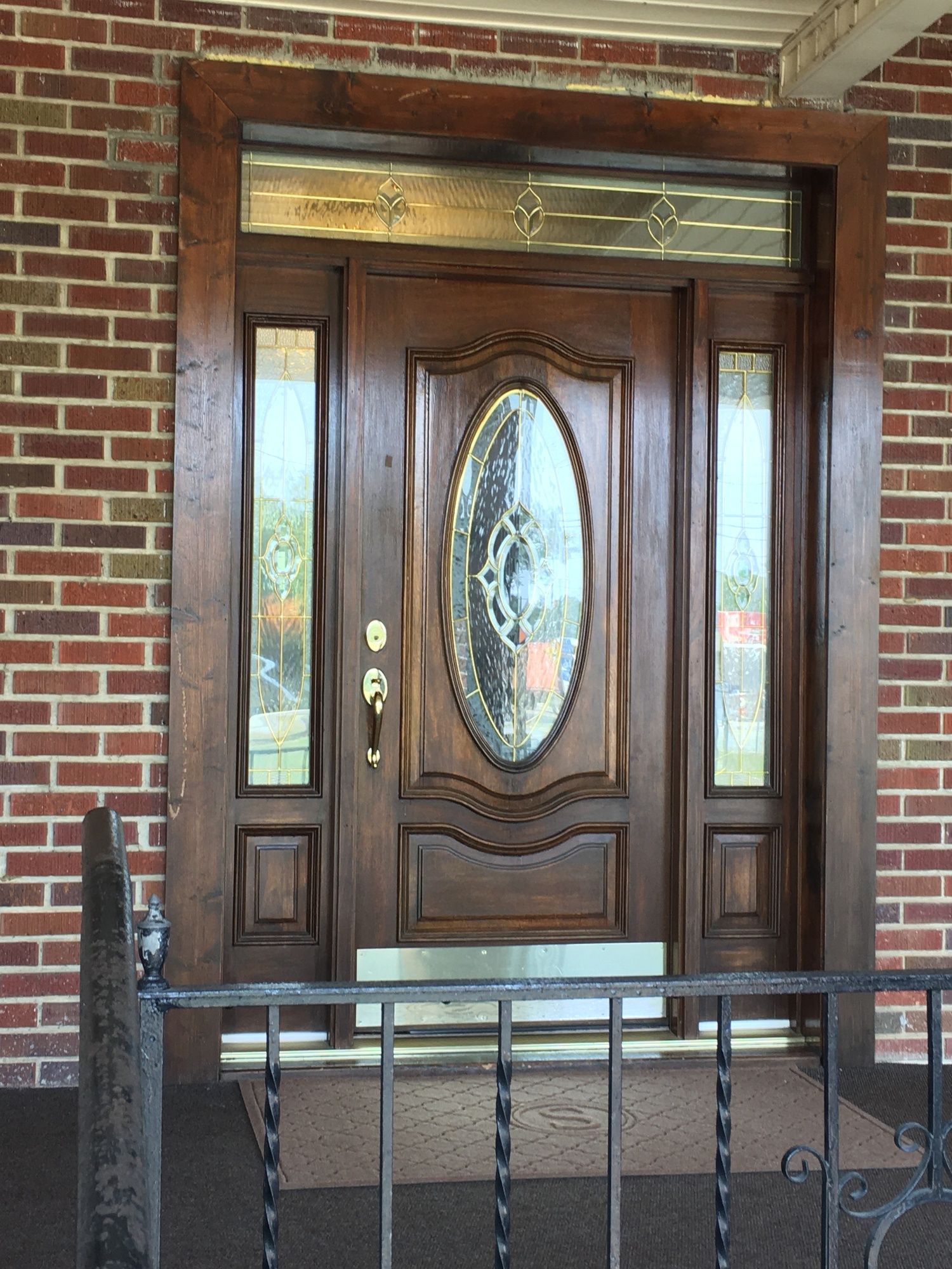 Front entrance with a dark wooden door, oval glass inset, and red brick walls behind a black railing.
