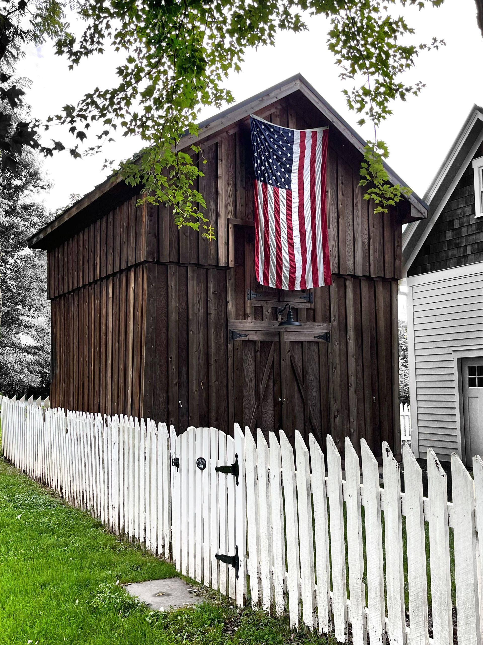Wooden barn with a large American flag hanging on it behind a white picket fence.