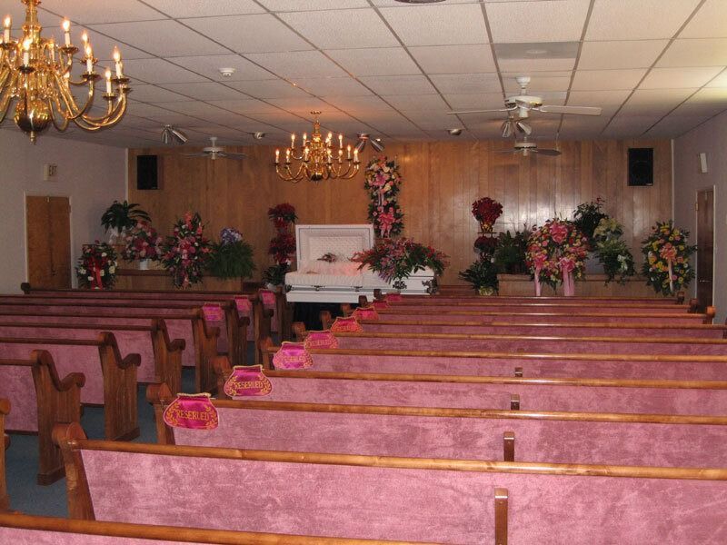 Small chapel with pink pews, floral arrangements, and a casket at the front.