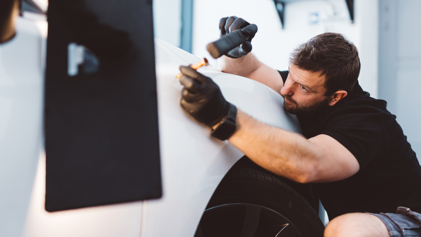 Paintless Dent Repair Person using a hammer to repair a white car panel, focused close-up in a garage.