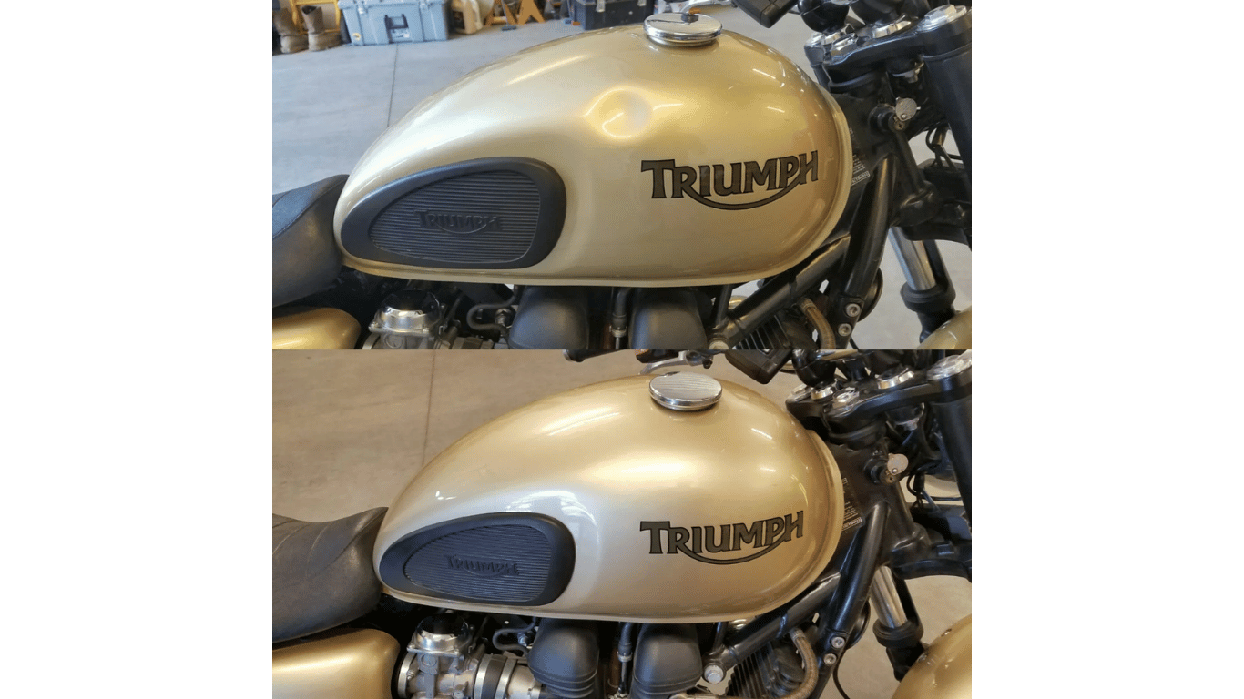 Two Triumph motorcycle fuel tanks, gold with black knee pads, stacked vertically in a garage.