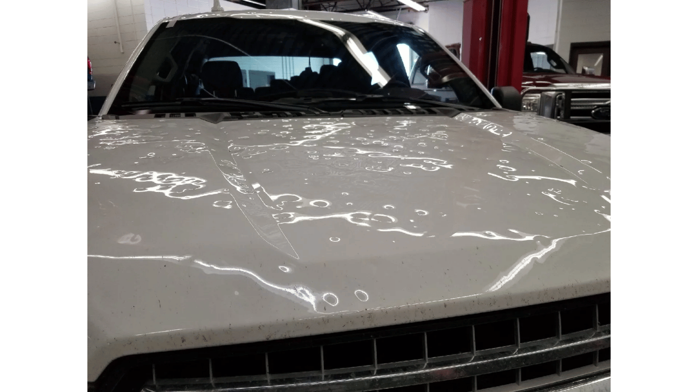 Front view of a white car with a dented hood inside a garage
