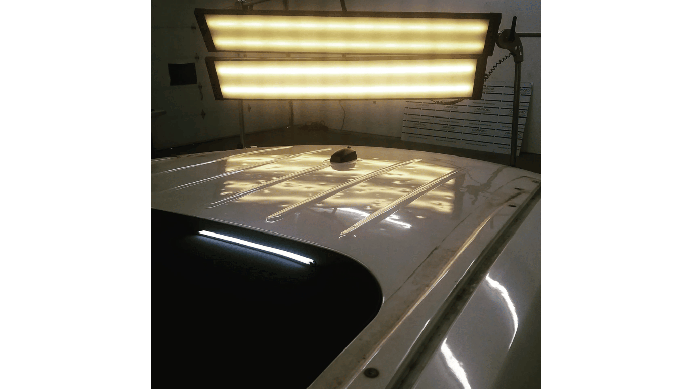 White car roof under bright shop lights in a garage, with reflections visible on the paint.
