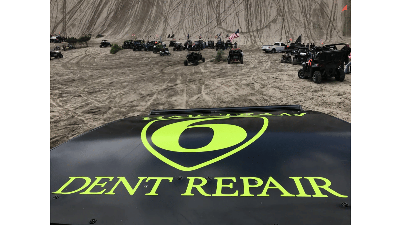 Black ATV hood with neon green Dent Repair logo in foreground, ATVs lined up on a sandy trail ahead