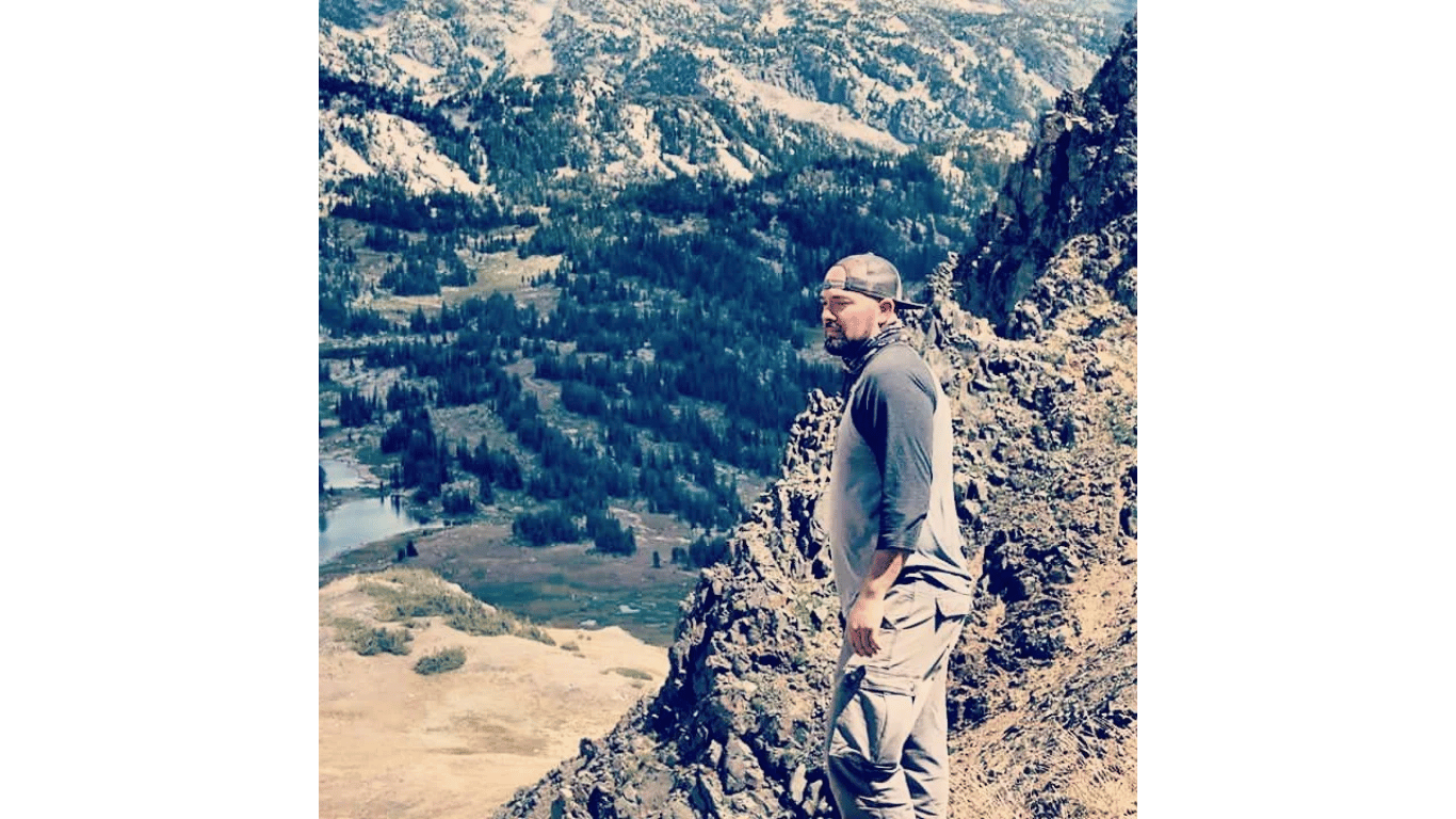 Person standing on a rocky ledge overlooking a forested mountain valley