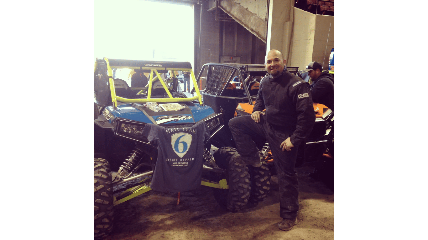 Man standing beside a blue off-road vehicle with large tires in a garage setting