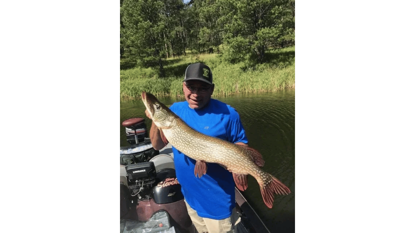 Person in a blue shirt holding a large fish outdoors near an ATV.