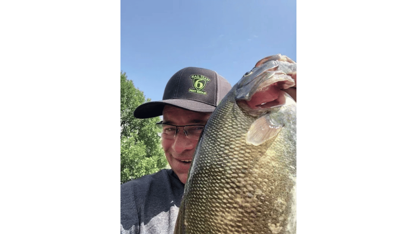 Person holding a large fish outdoors, wearing a cap and glasses.