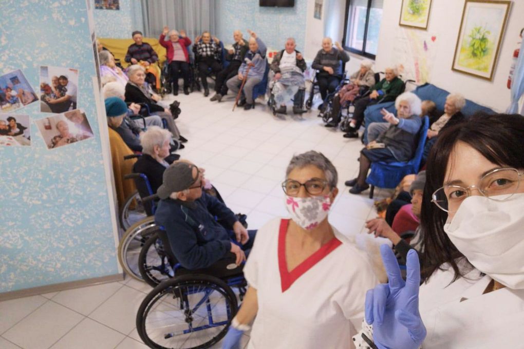 Un professionista del settore medico siede a un tavolo con tre persone, impegnate in un'attività in una stanza luminosa e accogliente.