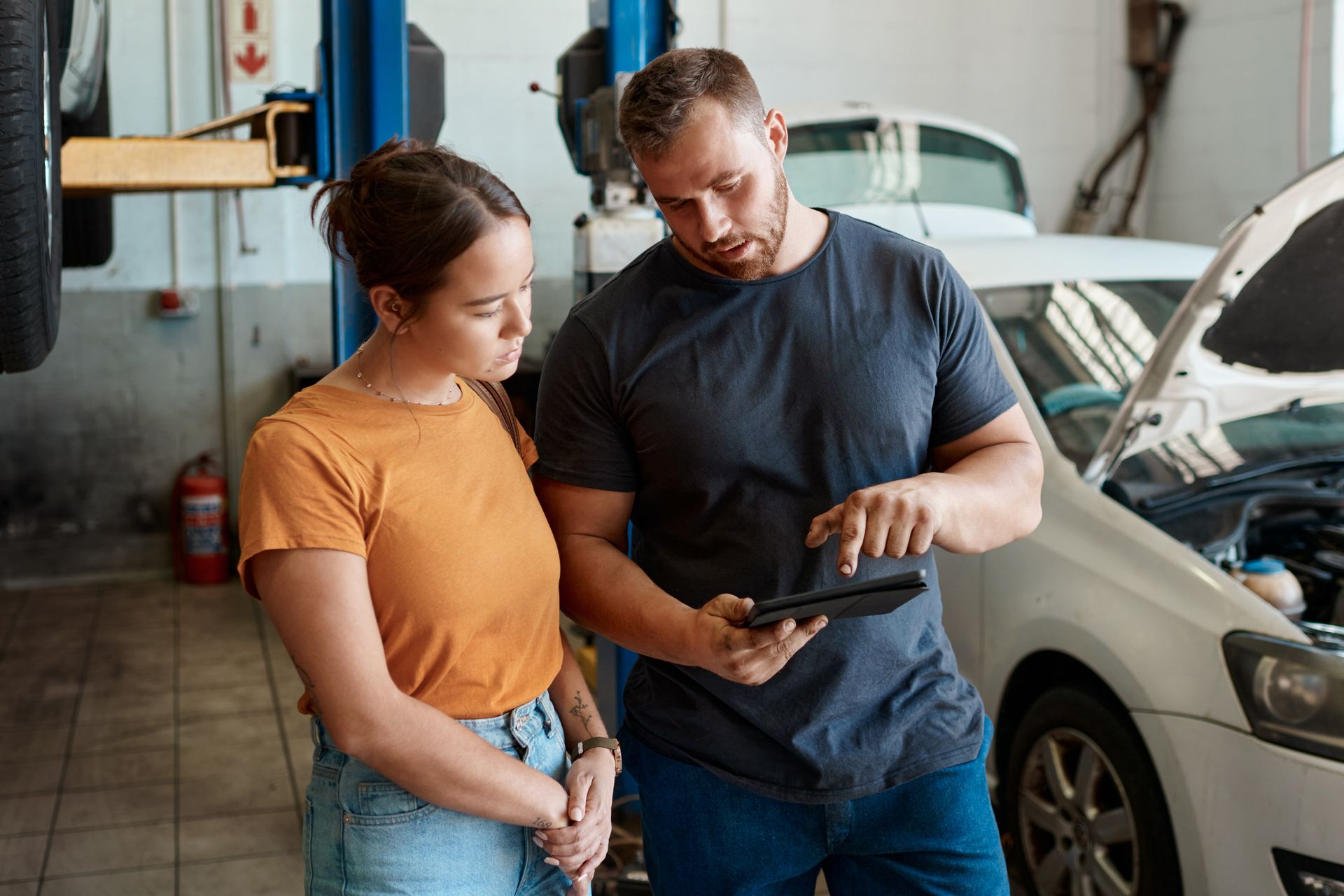 An auto mechanic is showing a customer her car diagnosis on a tablet in a repair shop.