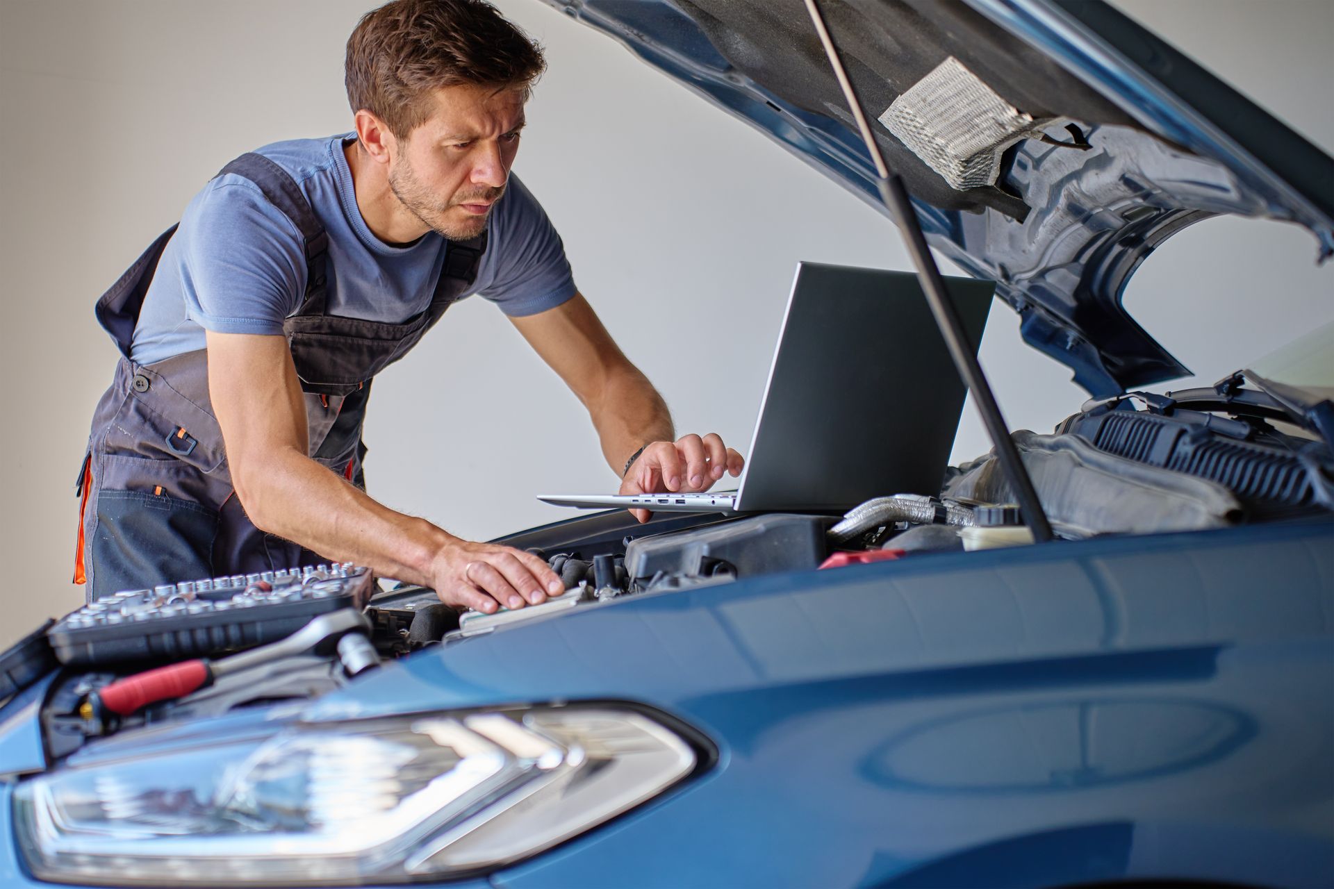 An auto mechanic is using a laptop for diagnostics of a vehicle engine in an auto repair shop.