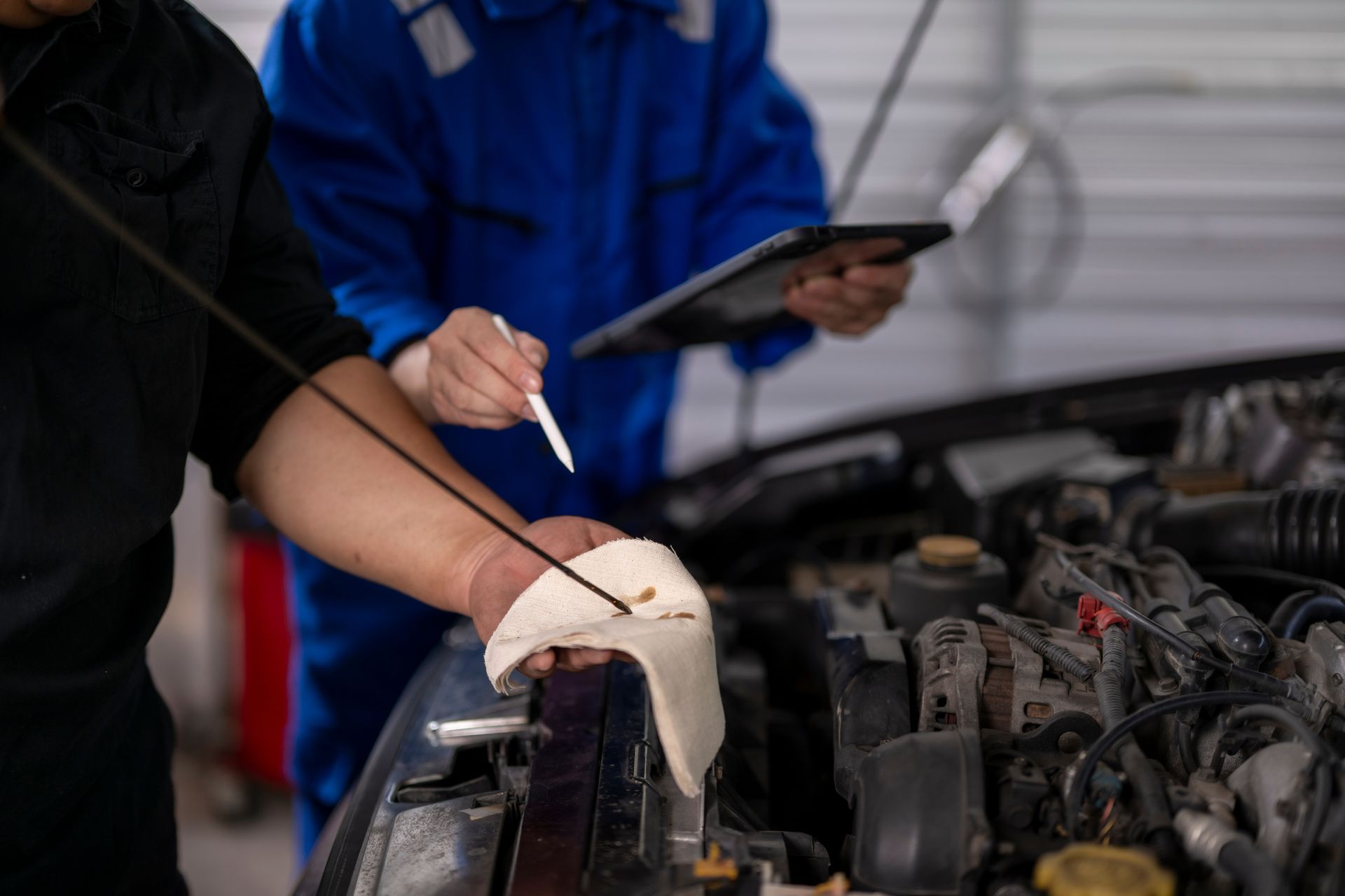 A close-up of two mechanics checking a car engine’s oil level with a tablet.