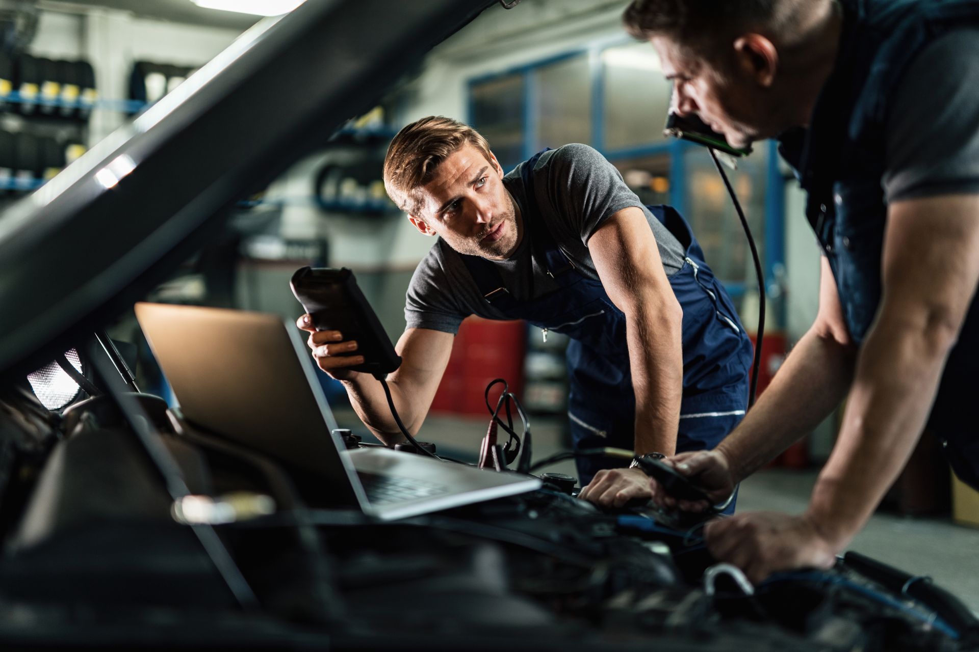 Auto mechanics talking while working on car diagnostics in a repair shop.