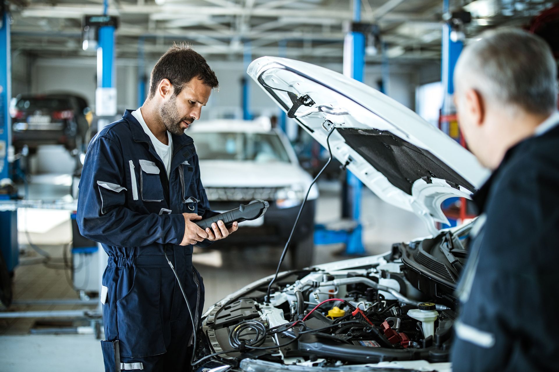 Mechanic using scan tool on car engine in shop for accurate automotive diagnostic services.
