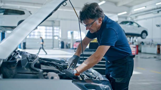 A mechanic performs automotive repair on a car in a garage, surrounded by tools and equipment.