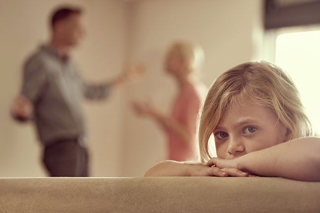 Unhappy child with parents arguing in background