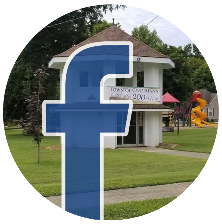 Blue Facebook logo over a town sign and building in a grassy park setting