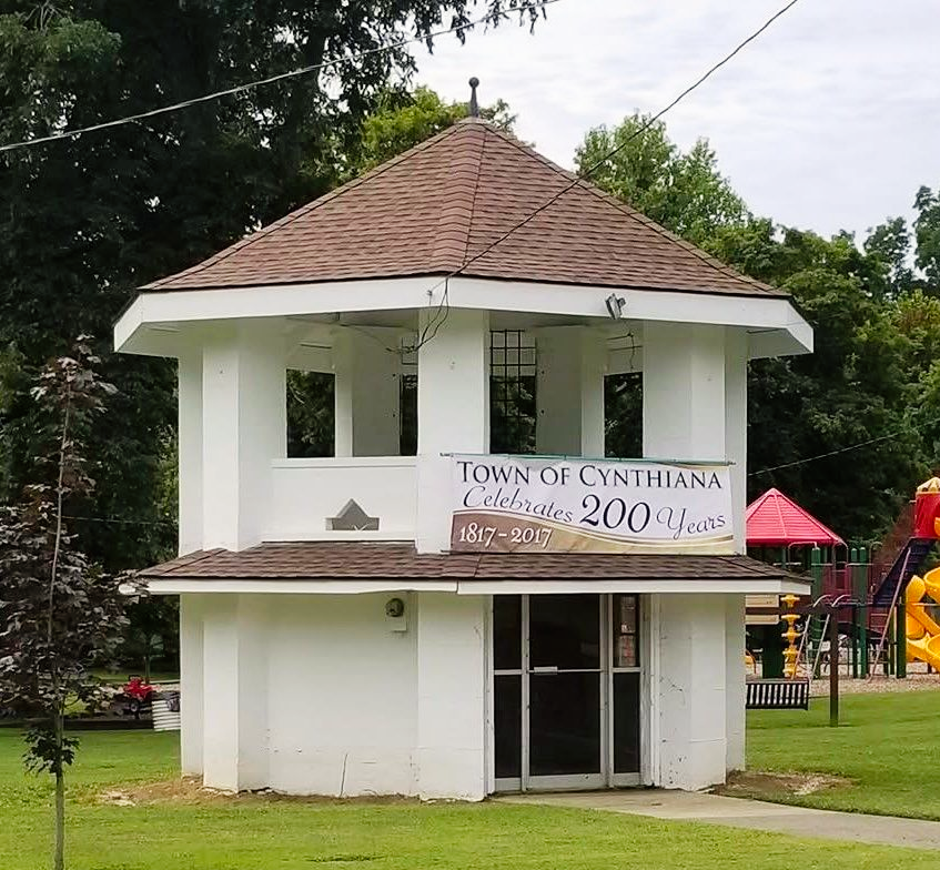 Small white town gazebo with sign reading “Town of Cynthiana 200 Years” in a grassy park