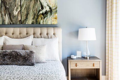 A bedroom with a bed , nightstand , lamp and painting on the wall.