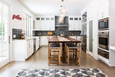 A kitchen with white cabinets , stainless steel appliances , a wooden table and stools.