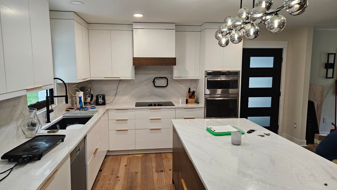 Modern white kitchen with island, wood floor, stainless appliances, and black glass door