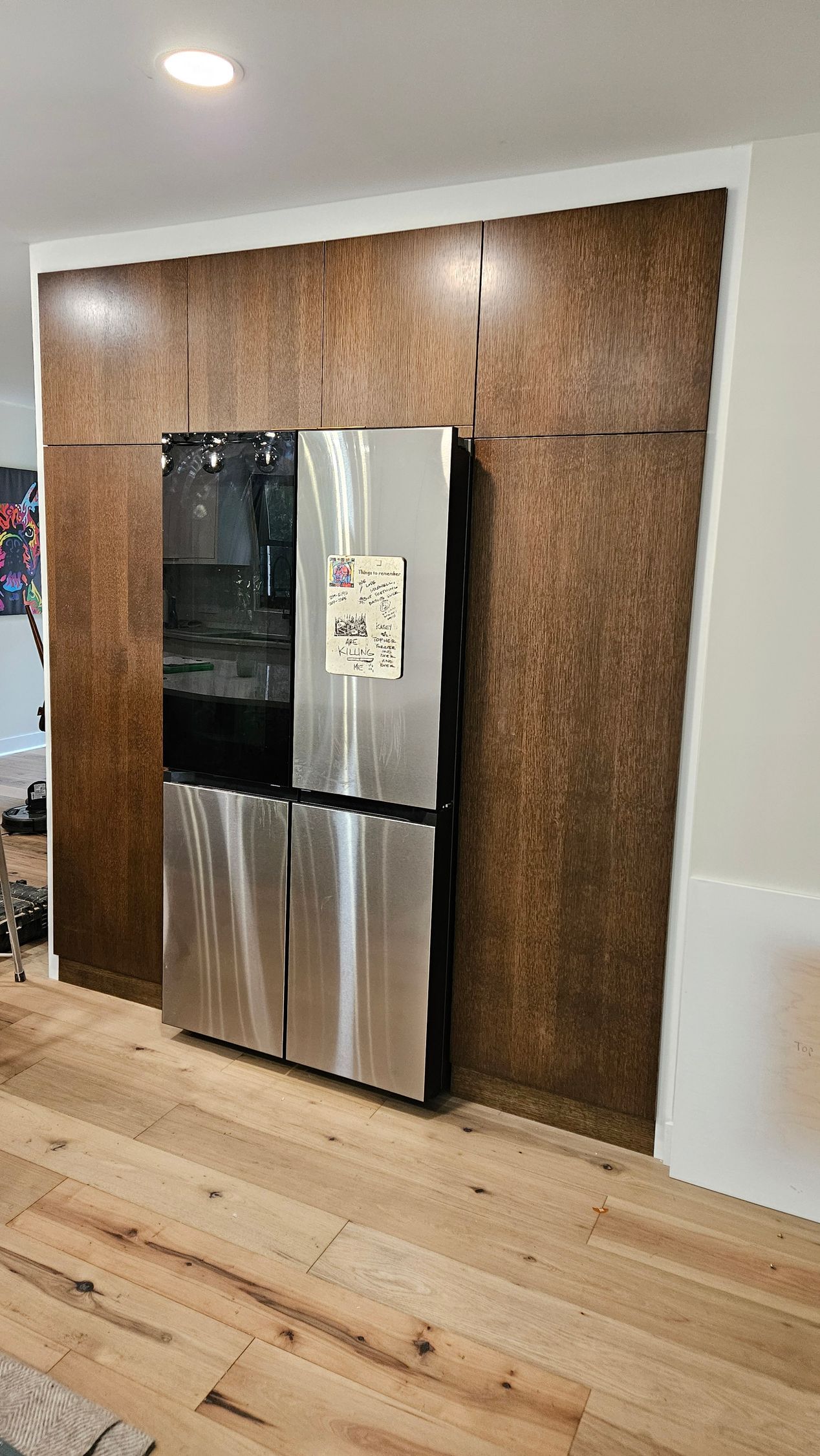 Stainless steel refrigerator against a textured brown wall in a bright room with light wood floors