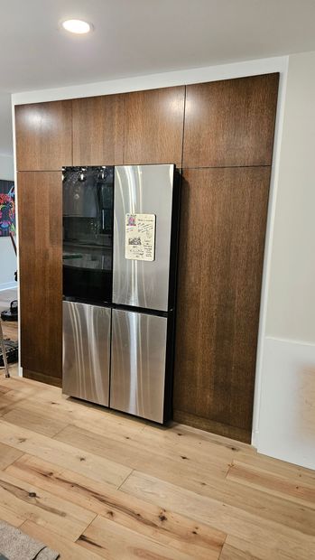 Stainless steel refrigerator built into a wood-paneled wall in a modern kitchen.