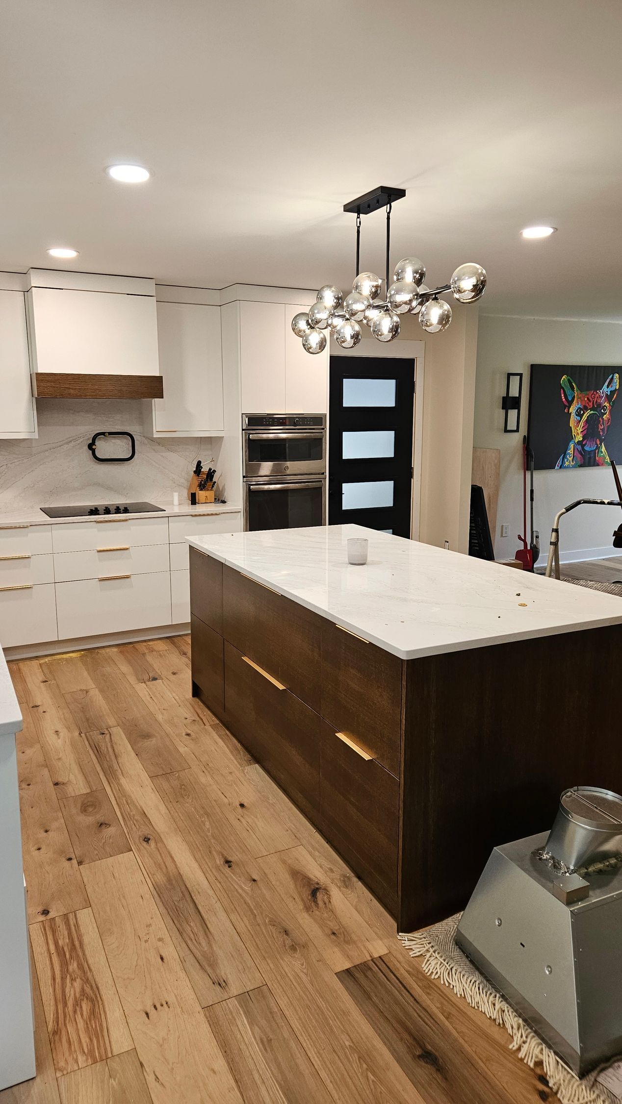 Modern kitchen with white cabinets, large island, wood floor, and pendant light over the center.