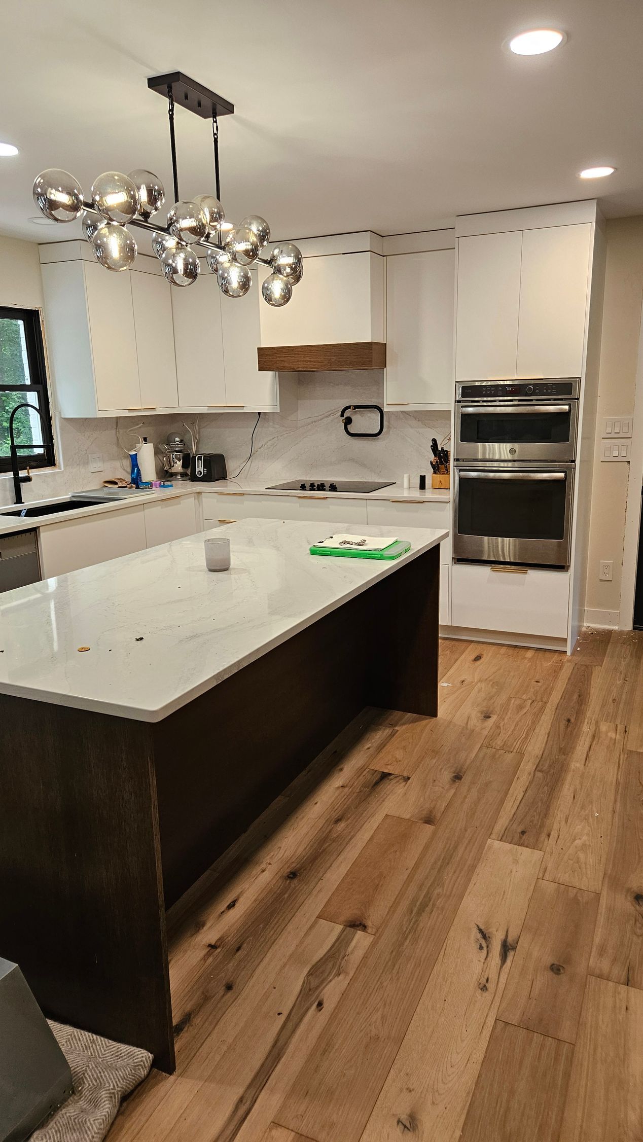 Modern kitchen with white island, dark cabinets, pendant light, and wood floors
