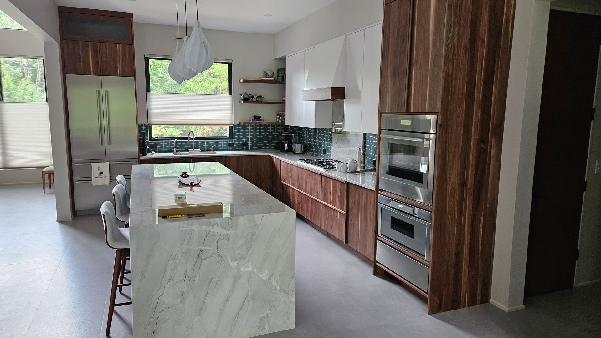 Modern kitchen with marble island, wood cabinets, stainless appliances, and a large window.