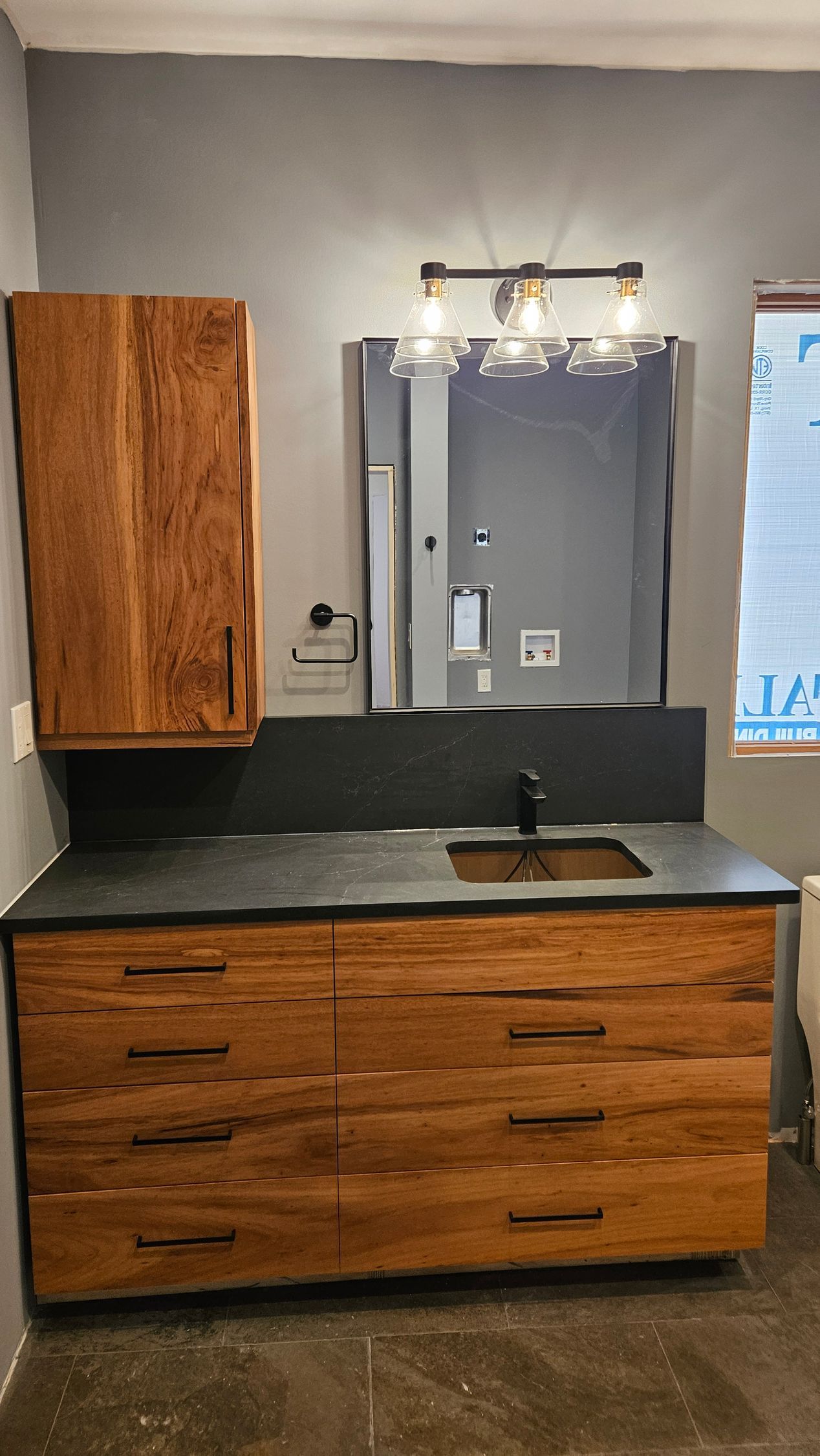 Bathroom vanity with wood cabinets, black countertop, sink, mirror, and wall light fixture