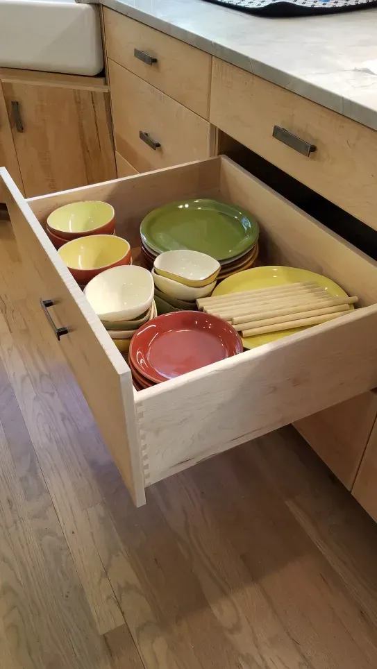 Open kitchen drawer with stacked colorful bowls and plates inside