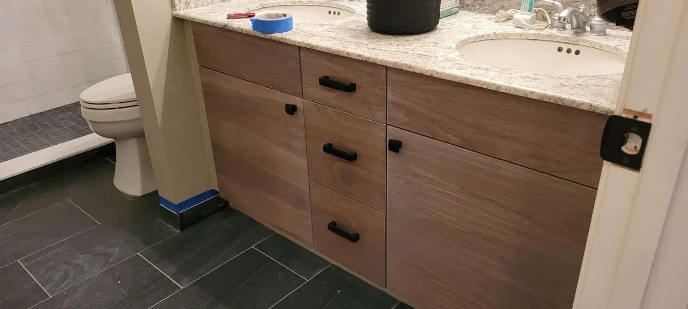 Bathroom vanity with wood cabinets, stone countertop, and dark tile floor near a toilet.