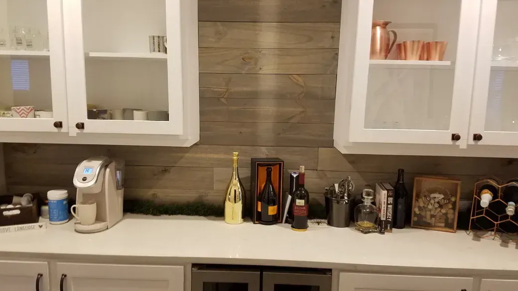 Kitchen counter with assorted bottles and containers beneath white cabinets and a wood backsplash