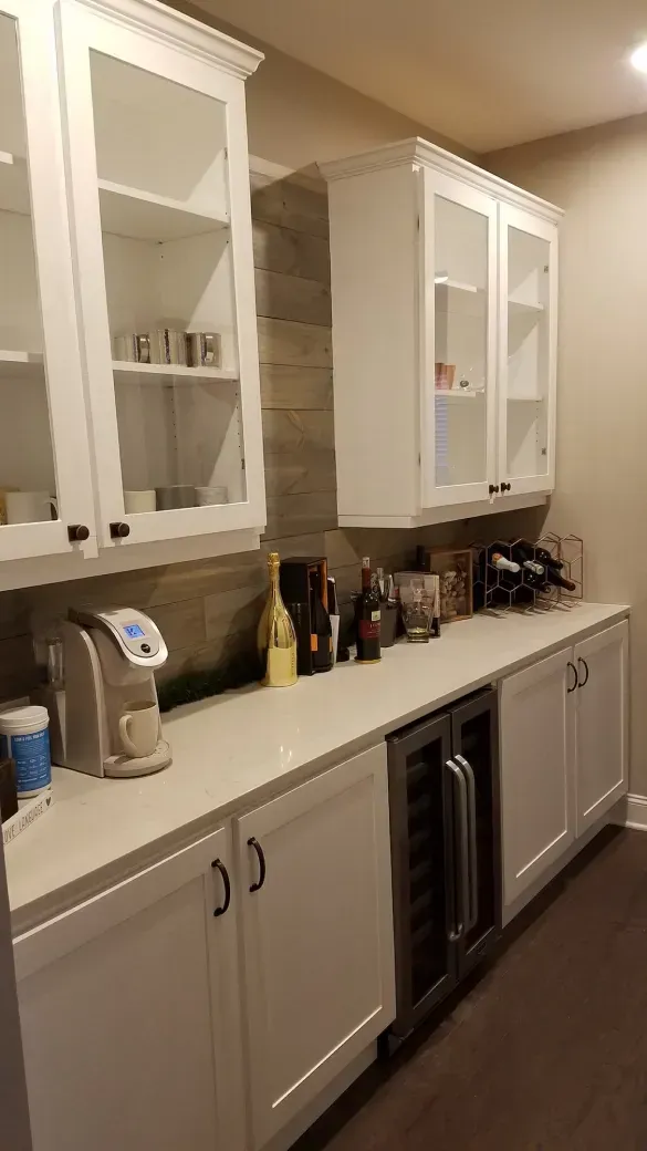 White kitchen cabinets and countertop with coffee maker, bottles, and a wine cooler beneath mirrored cabinet doors