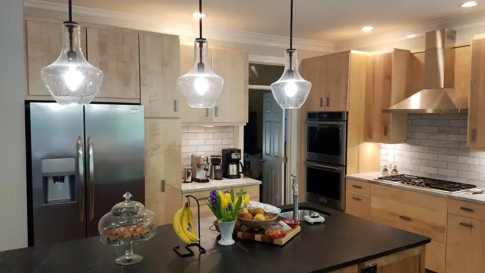 Modern kitchen with stainless steel appliances, wood cabinets, island, and pendant lights; fruit bowl on counter