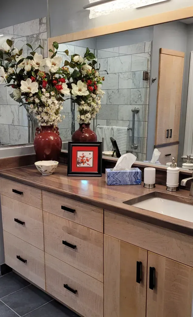 Bathroom vanity with a red vase of flowers, framed photo, tissue box, and sink under a large mirror