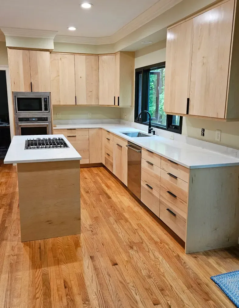Modern kitchen with light wood cabinets, white countertops, island stove, and hardwood floors.