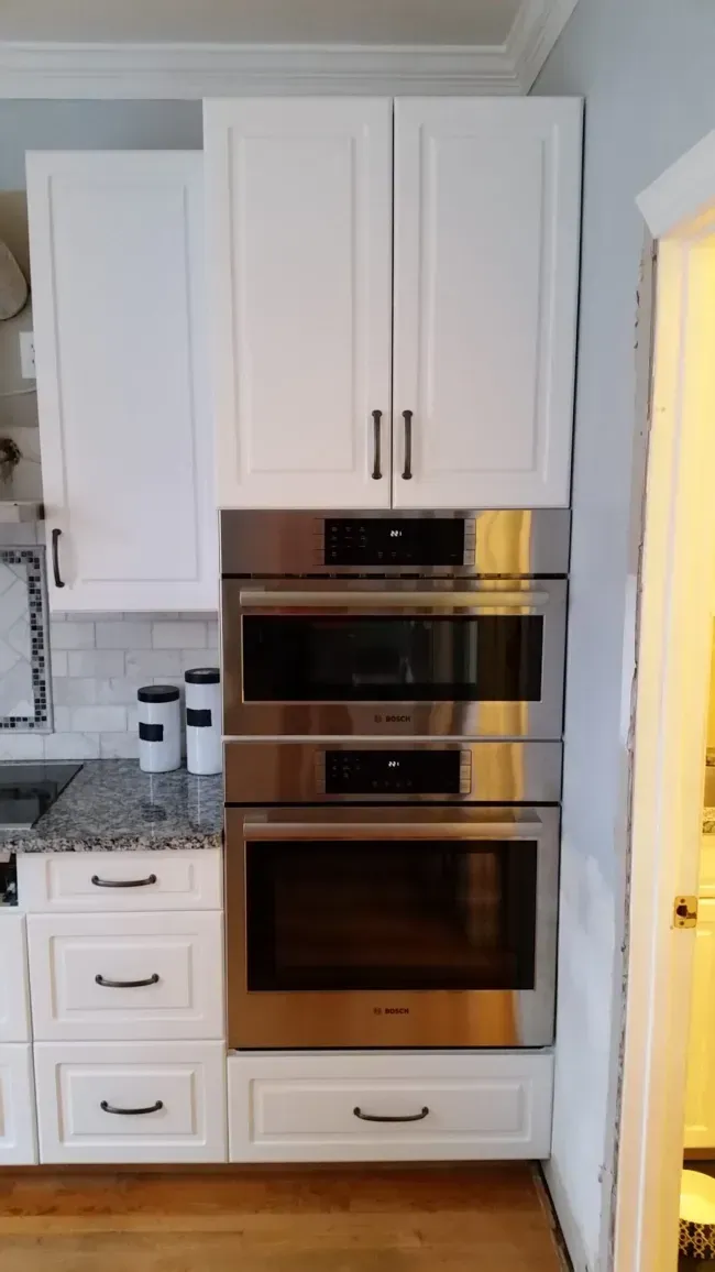 White kitchen cabinets with built-in stainless steel double oven and microwave stack.