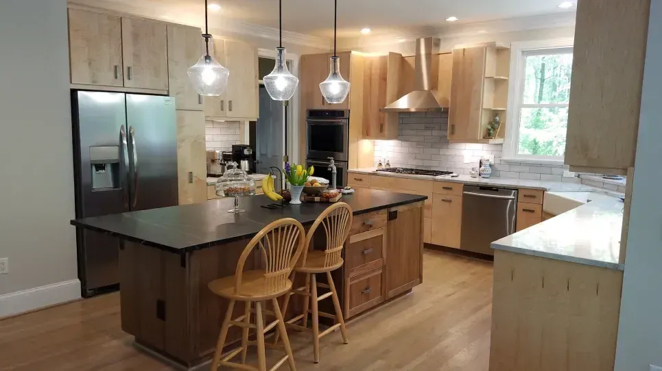 Modern kitchen with wood cabinets, island with stools, stainless steel fridge, and pendant lights