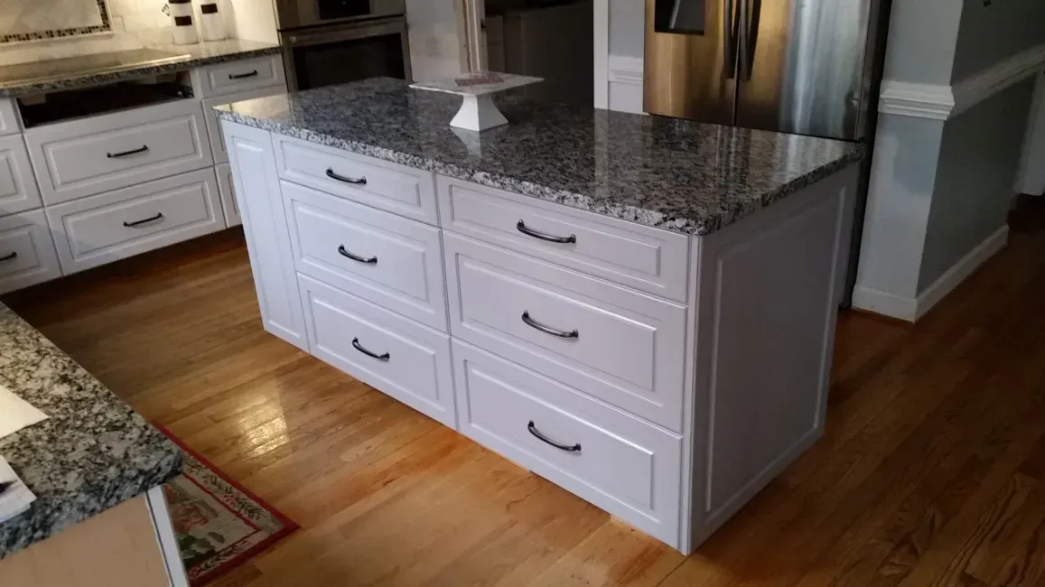 White kitchen island with granite countertop and drawers on a hardwood floor