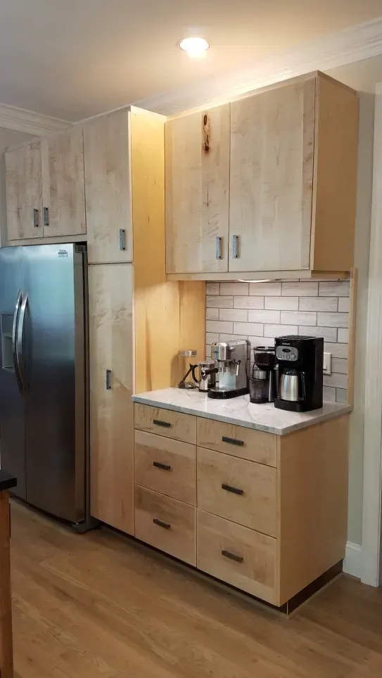 Kitchen nook with light wood cabinets, stainless fridge, white backsplash, and coffee maker on countertop