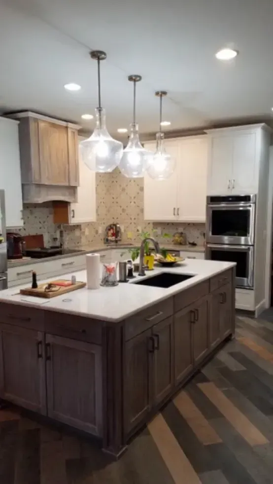 Modern kitchen with large island, white cabinets, stainless double oven, and pendant lights above.