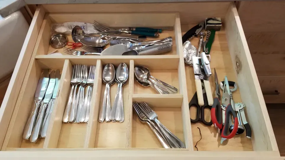 Wooden kitchen drawer organizer with neatly arranged silverware, serving utensils, and cooking tools